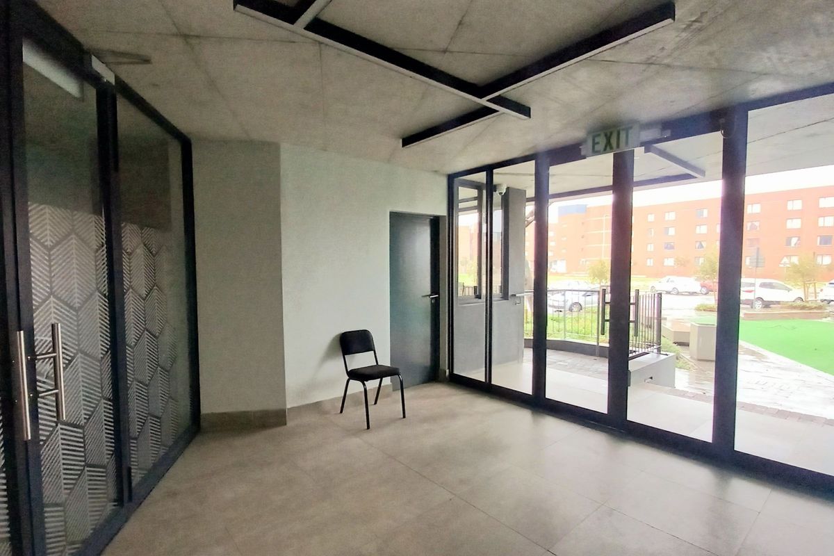 Modern apartment entrance foyer featuring exposed concrete ceilings, large glass sliding doors, and neutral tiled flooring, providing a bright and contemporary welcome area.