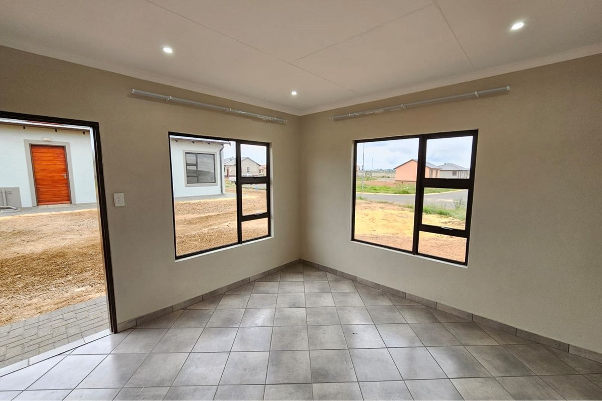 A bright, empty living area featuring neutral tiled flooring, modern aluminium-framed windows, and recessed ceiling downlights, offering a clean and versatile space.
