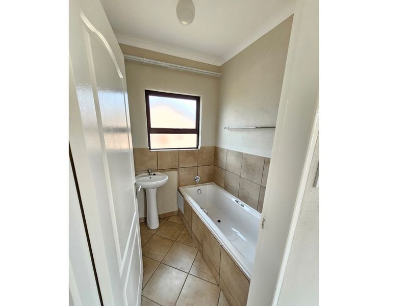 A compact bathroom featuring a tiled bathtub, pedestal basin, and neutral wall tiles, providing a functional and clean space.