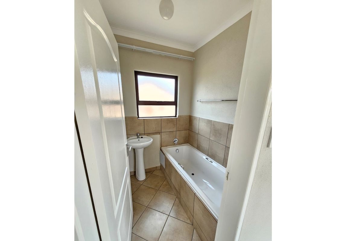 A compact bathroom featuring a tiled bathtub, pedestal basin, and neutral wall tiles, providing a functional and clean space.