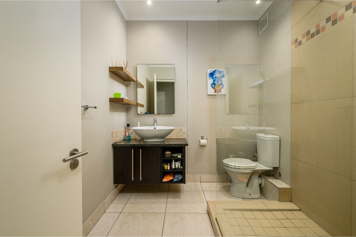Modern bathroom featuring a floating vanity with vessel sink, glass-enclosed shower, and neutral floor tiling.