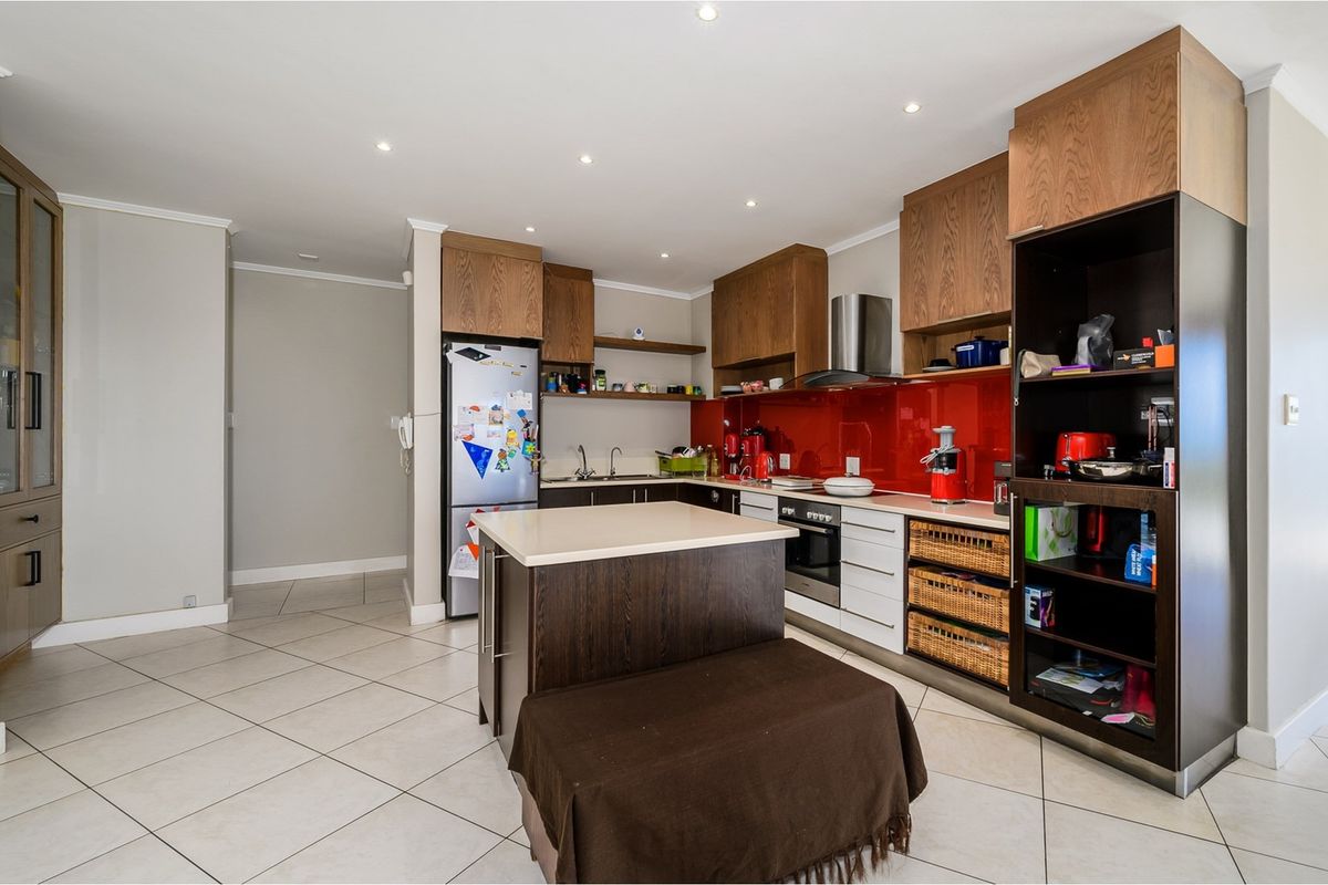 Modern kitchen featuring a central island, built-in oven, extractor fan, and vibrant red glass splashback with ample wooden cabinetry.