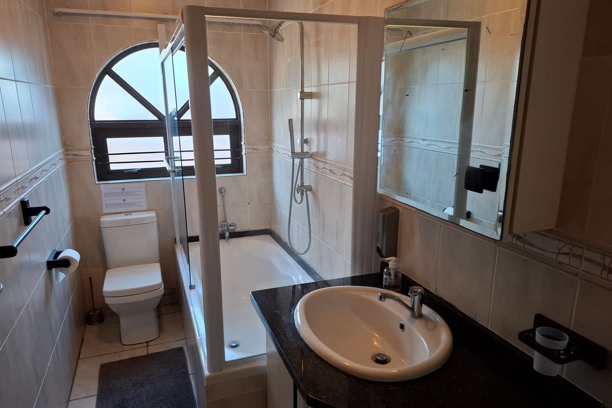 A functional bathroom featuring a shower-over-bath combination, a vanity with a granite countertop, and an arched window providing natural light.