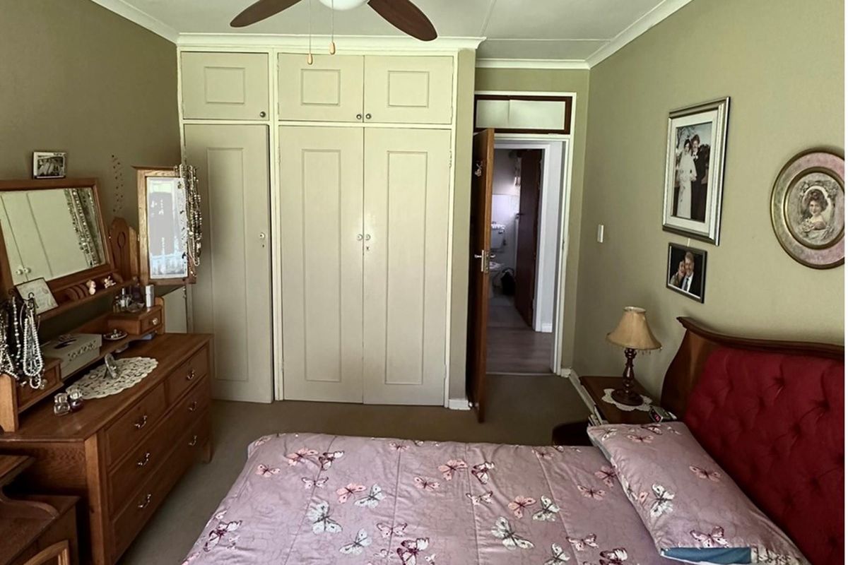 A bedroom featuring built-in cupboards and a ceiling fan, with an adjacent doorway leading to a bathroom area.