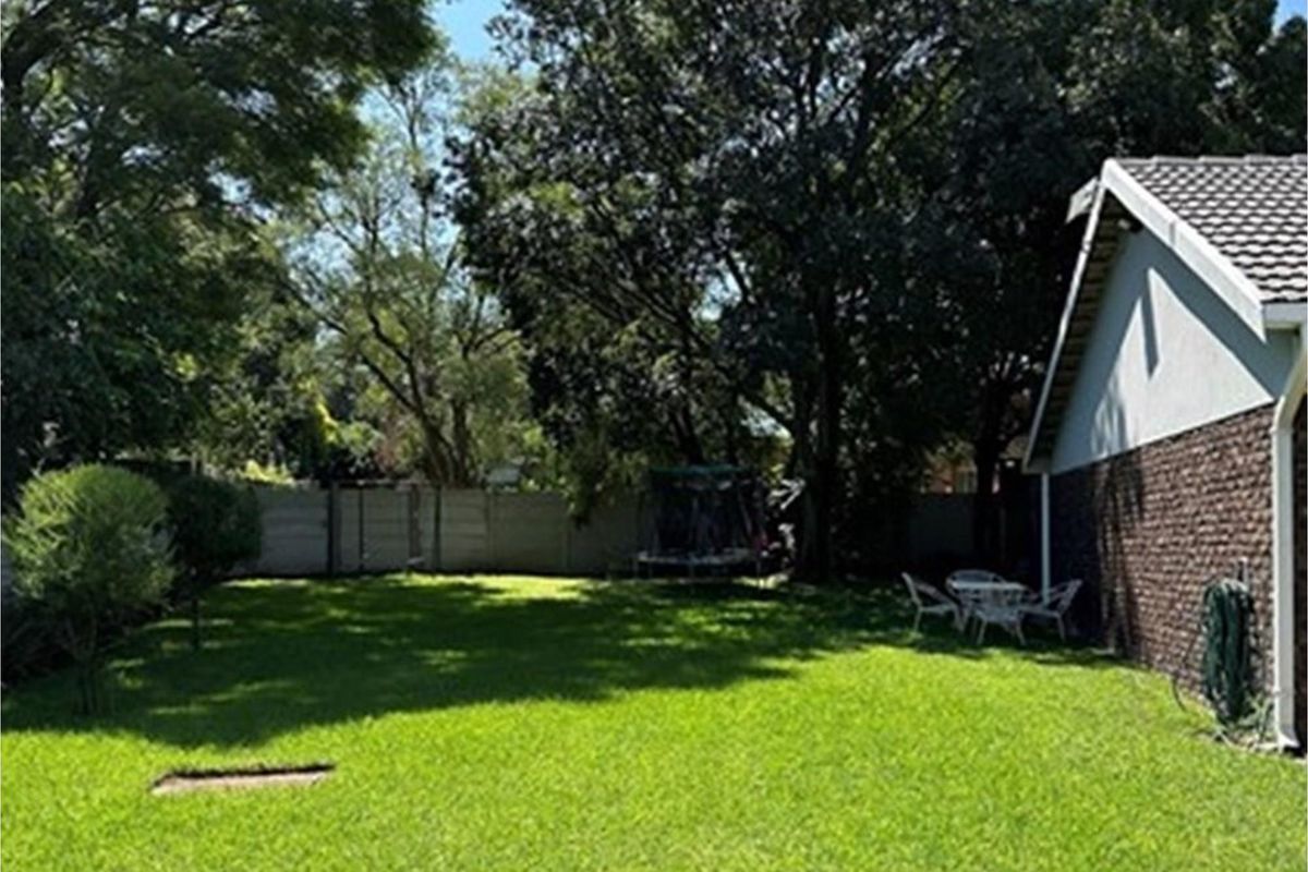 A spacious rear garden featuring a well-maintained lawn, mature trees, and perimeter boundary walling, providing a private outdoor space.
