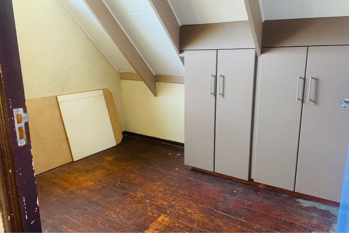 An attic-style bedroom featuring sloped ceilings, built-in cabinetry, and original timber flooring.