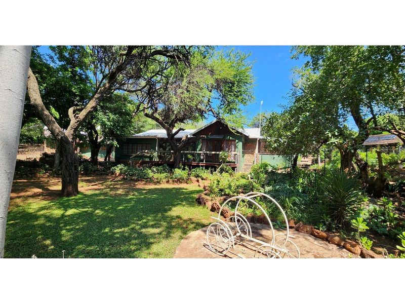A view of the rear exterior of the farmhouse, featuring a wooden deck, established garden, and mature trees.