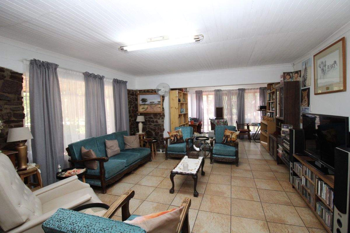 Spacious living room featuring rustic stone wall accents, tiled flooring, and large windows allowing for ample natural light.