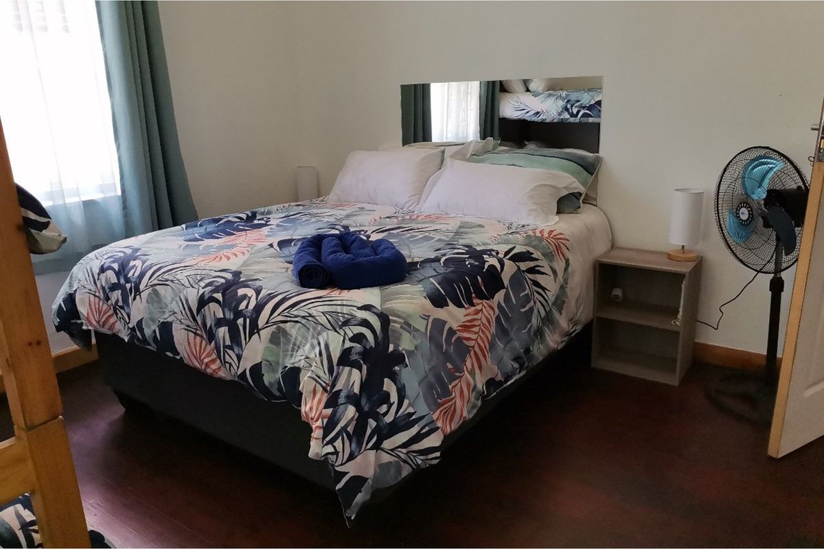 A bedroom featuring dark laminate flooring and a built-in mirror headboard, providing a functional space with natural light from the window.