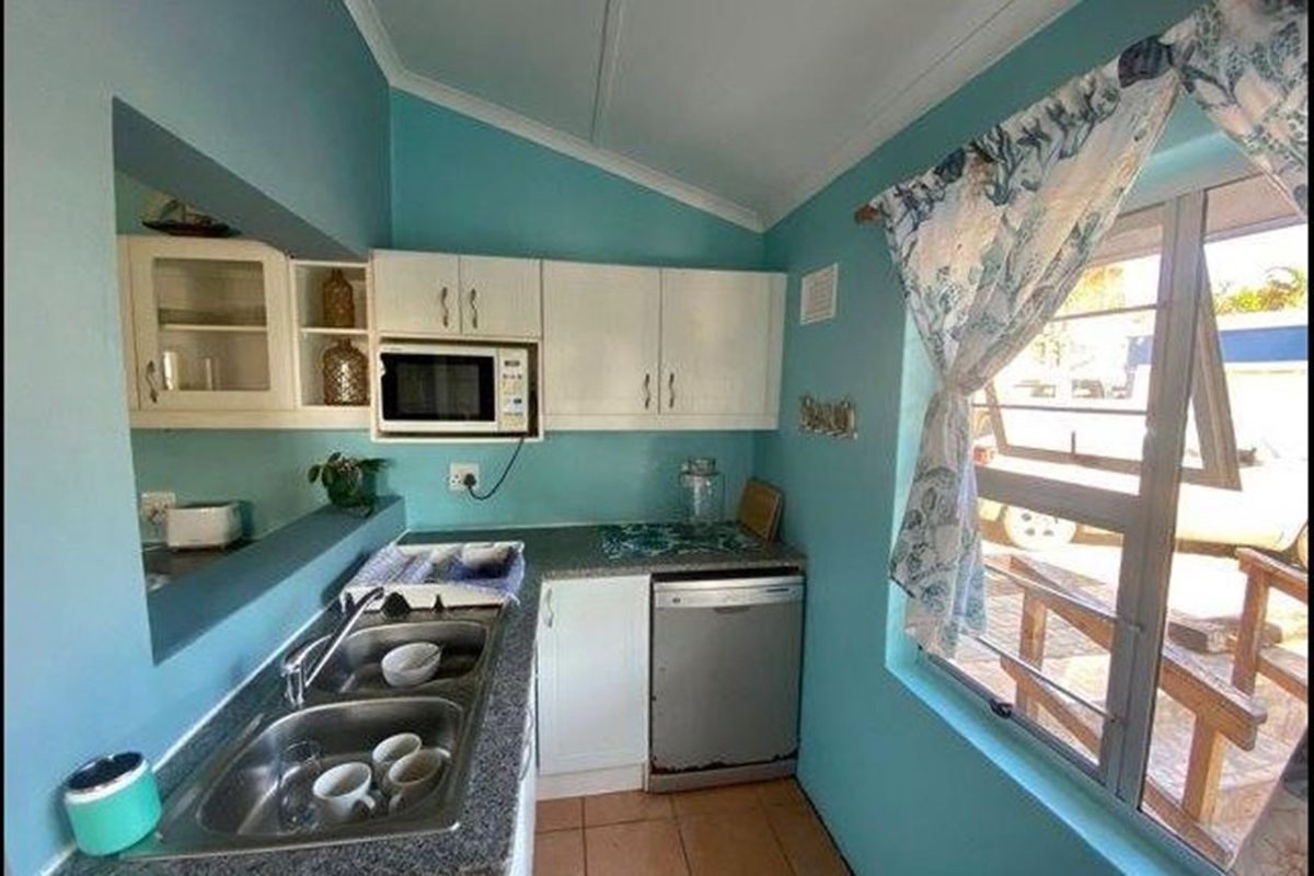Compact kitchen featuring white built-in cabinetry, a double stainless steel sink, built-in microwave, and tiled flooring with natural light from a side window.