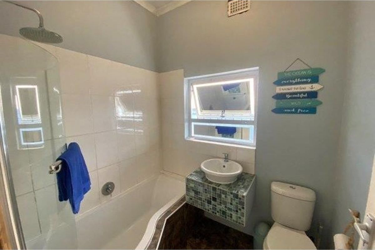 A functional bathroom featuring a bathtub with an overhead shower, a vessel sink on a tiled vanity, and a toilet.