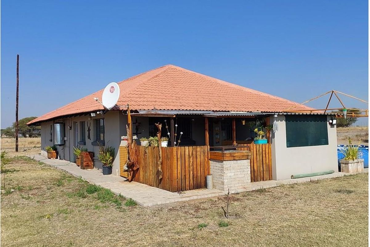 Rear view of a farm dwelling featuring a tiled roof, a covered patio area with timber fencing, and a built-in outdoor braai structure.