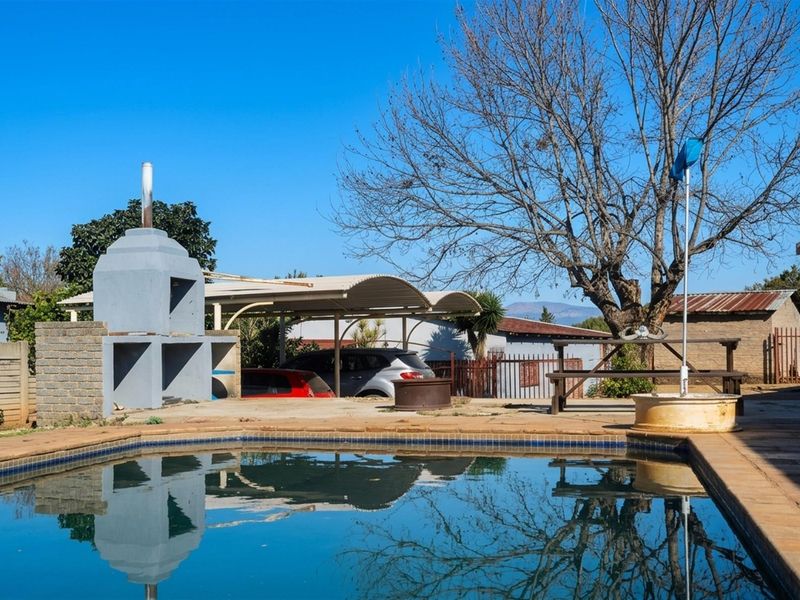 Outdoor pool area featuring a built-in braai, paved surround, and a double carport, set within a farm property environment.