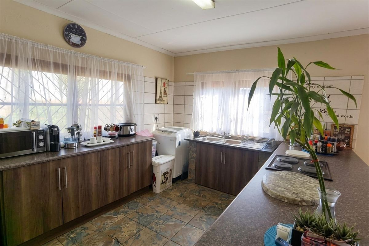 A functional kitchen featuring wood-look cabinetry, laminate countertops, a double basin sink, and an integrated electric hob with tiled splashbacks.