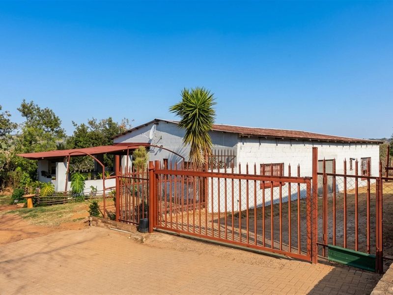 Front view of a farm property featuring a paved driveway, secure metal perimeter fencing, and a covered patio area.