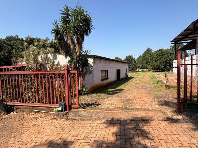 A view of the farm property entrance featuring a brick paved driveway, metal security gate, and a long outbuilding with painted masonry walls.