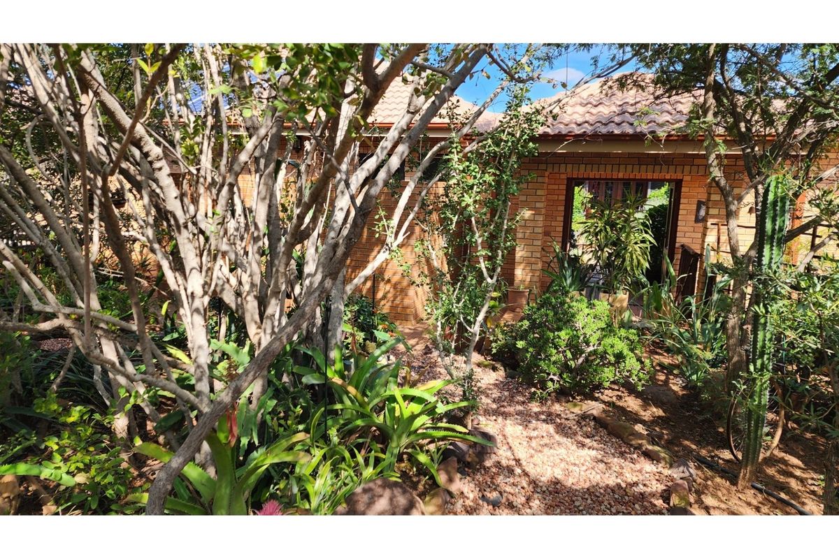 A view of the property's exterior rear garden area, featuring established landscaping, brick facade, and a tiled roof.