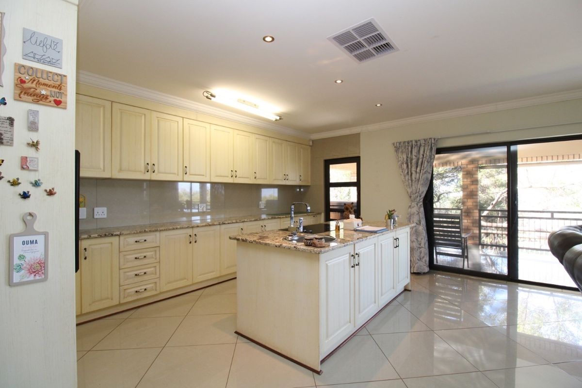 Spacious kitchen featuring cream cabinetry, granite countertops, a central island with a sink, and direct access to an outdoor patio area.
