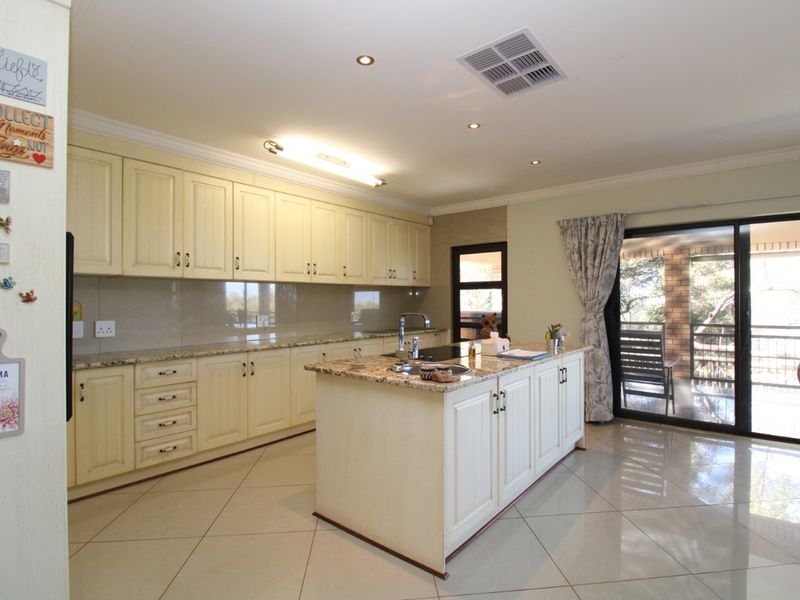 Spacious kitchen featuring cream cabinetry, granite countertops, a central island with a sink, and direct access to an outdoor patio area.