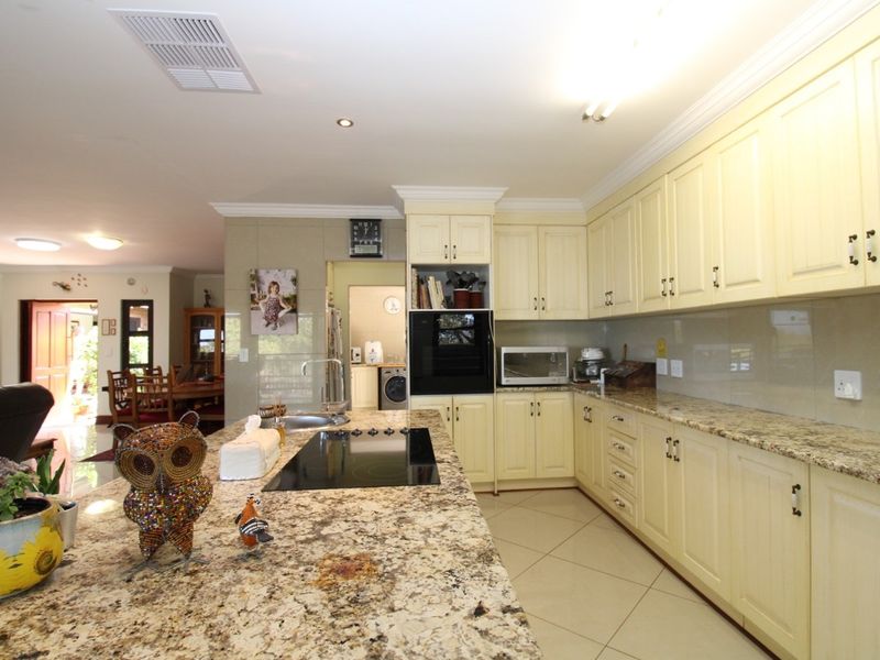 Spacious kitchen featuring granite countertops, cream-colored cabinetry, a central island with a built-in hob, and integrated oven, flowing into an open-plan living area.