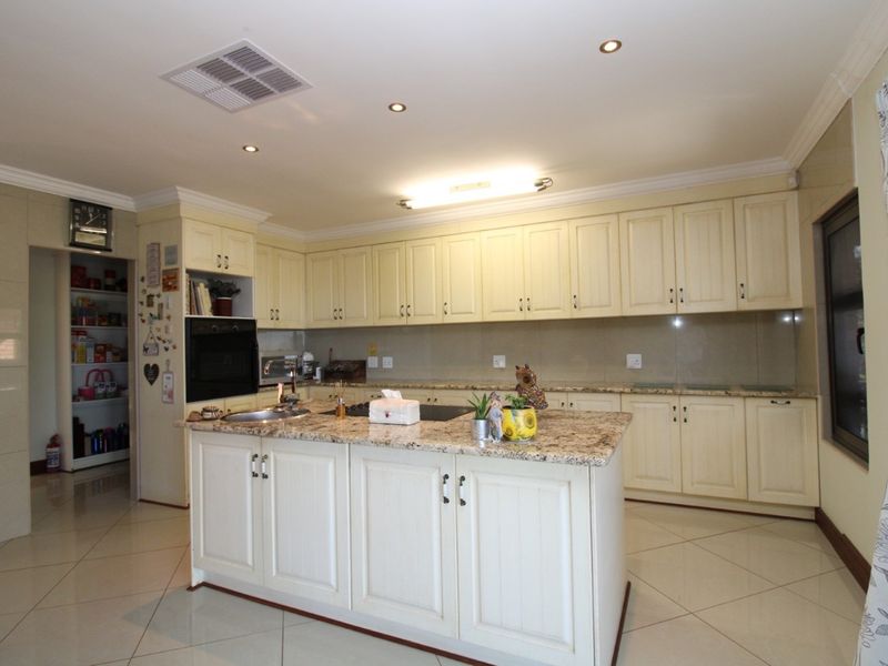 Spacious kitchen featuring cream cabinetry, granite countertops, a central island with a built-in hob, and an adjacent walk-in pantry.