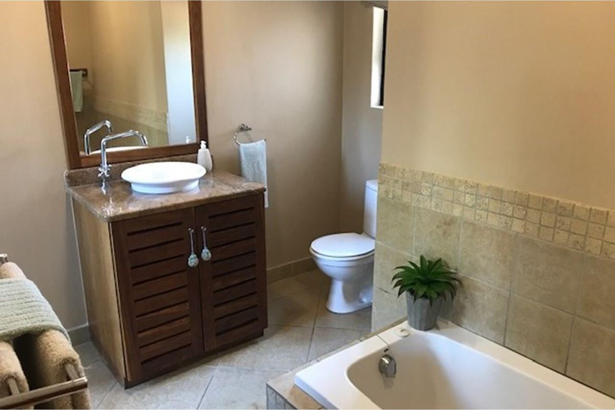 A functional bathroom featuring a vanity with a vessel sink, a toilet, and a tiled bathtub surround.