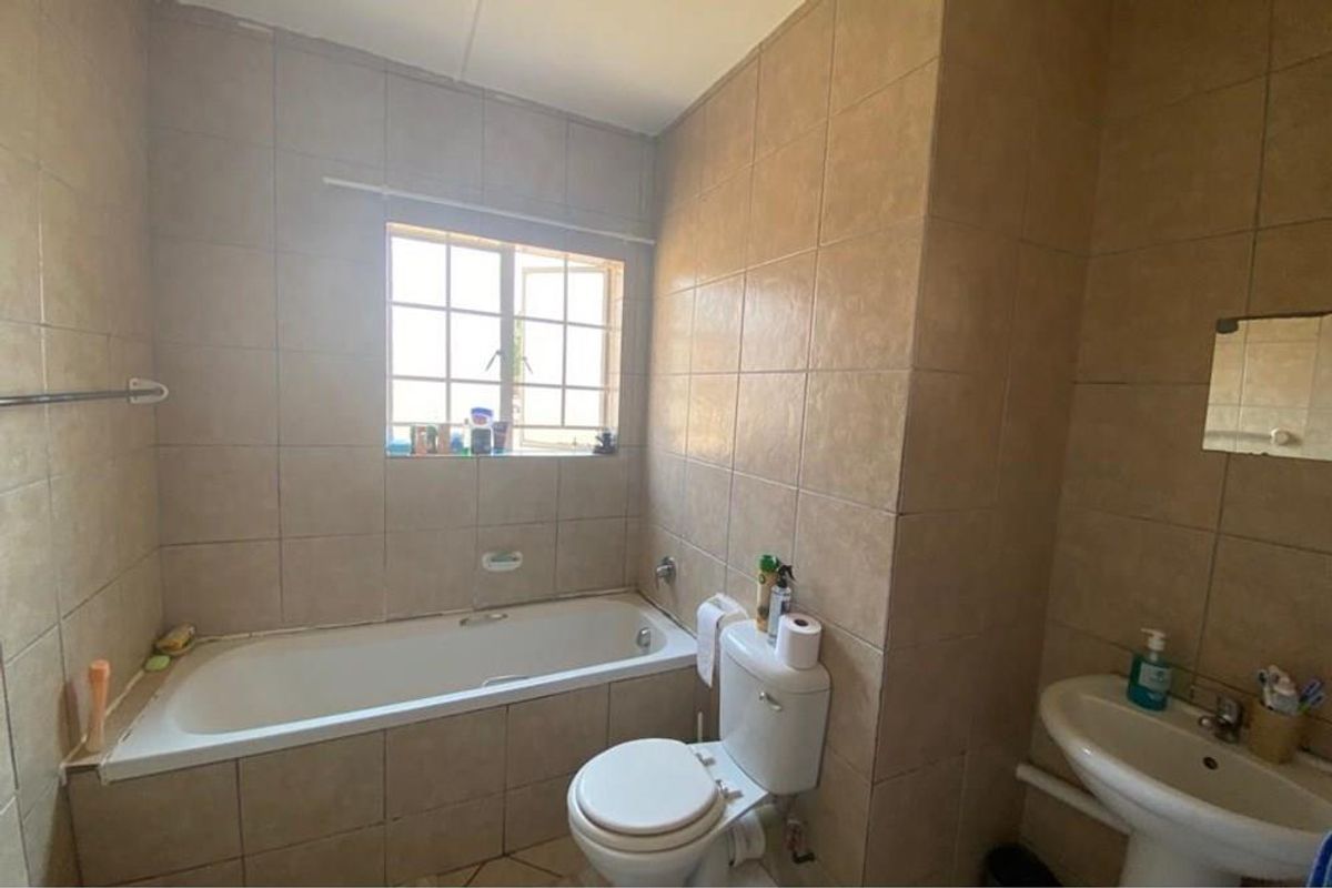 A functional bathroom featuring a built-in bathtub, pedestal basin, and tiled walls, offering a practical layout with natural light from the window.