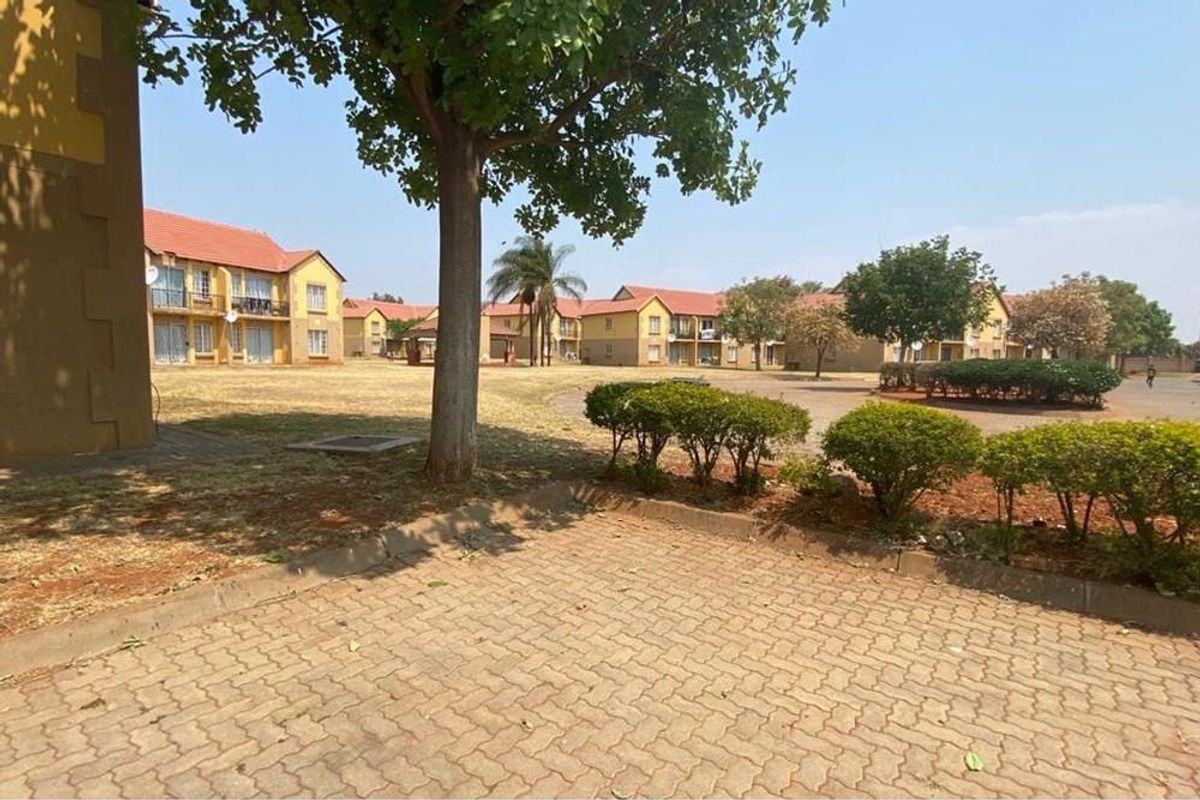 A view of the apartment complex grounds featuring paved walkways, established trees, and communal garden areas between the residential buildings.