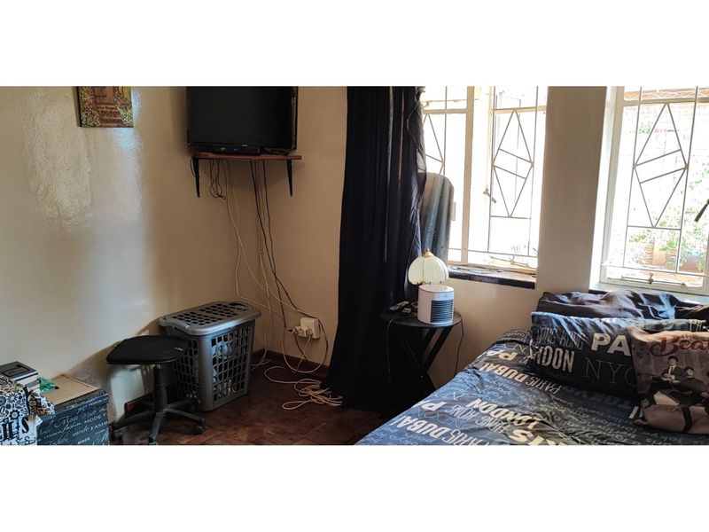 A bedroom featuring parquet flooring and security bars on the windows, currently showing signs of wear and exposed electrical cabling.