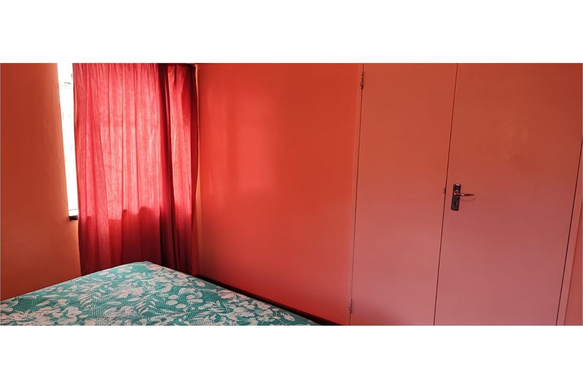 A bedroom featuring a built-in cupboard and window with curtains.