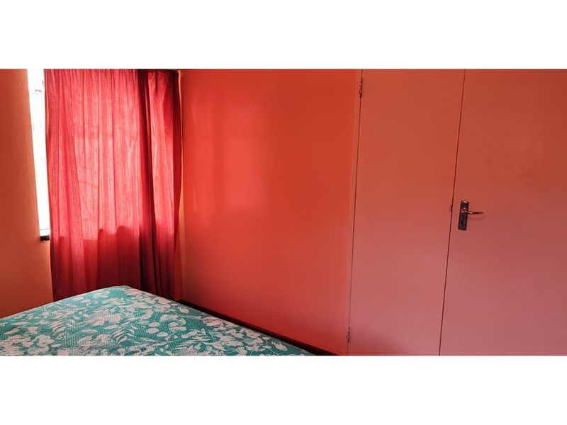 A bedroom featuring a built-in cupboard and window with curtains.