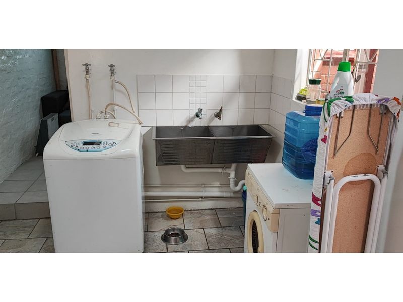 A functional laundry area featuring a double stainless steel sink, tiled splashback, and dedicated plumbing connections for washing machines.