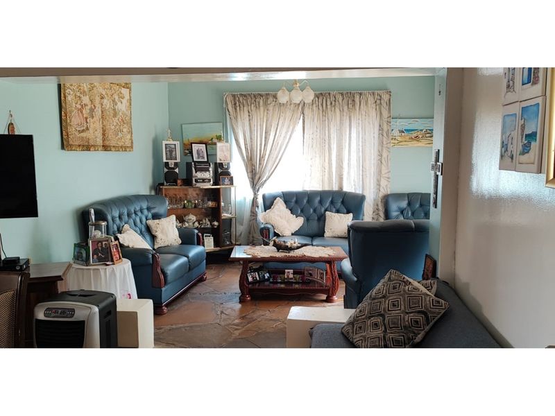 A living room featuring traditional flagstone flooring and large windows with curtains, offering a dated but functional living space.