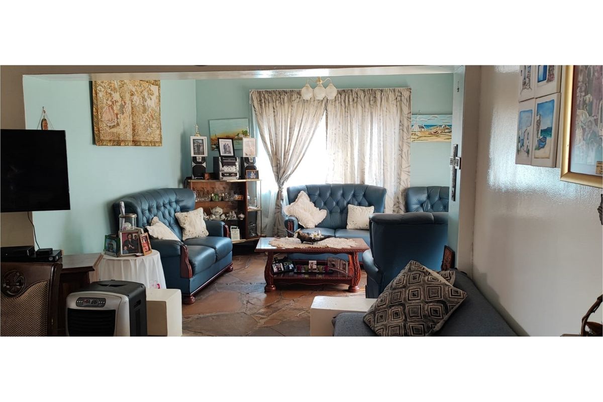 A living room featuring traditional flagstone flooring and large windows with curtains, offering a dated but functional living space.