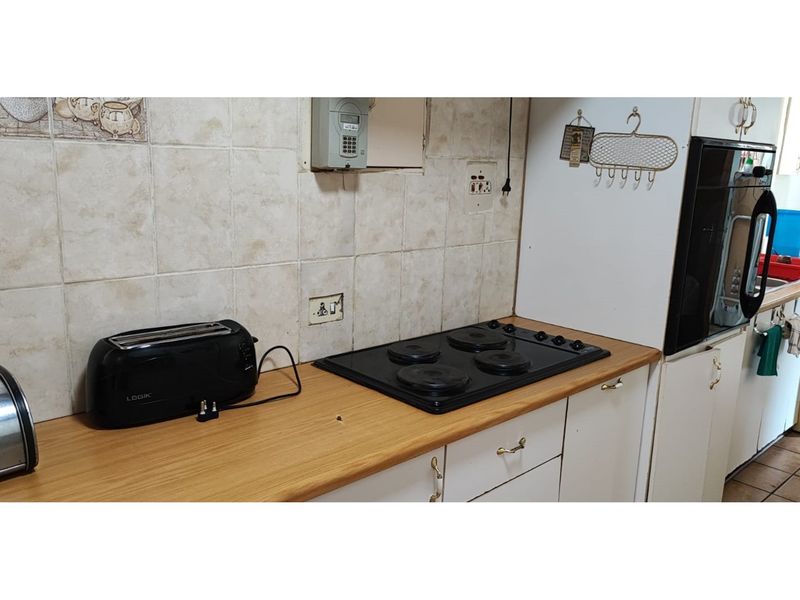 A functional kitchen area featuring a built-in electric hob, oven, laminate countertops, and tiled backsplash with ample cabinetry for storage.