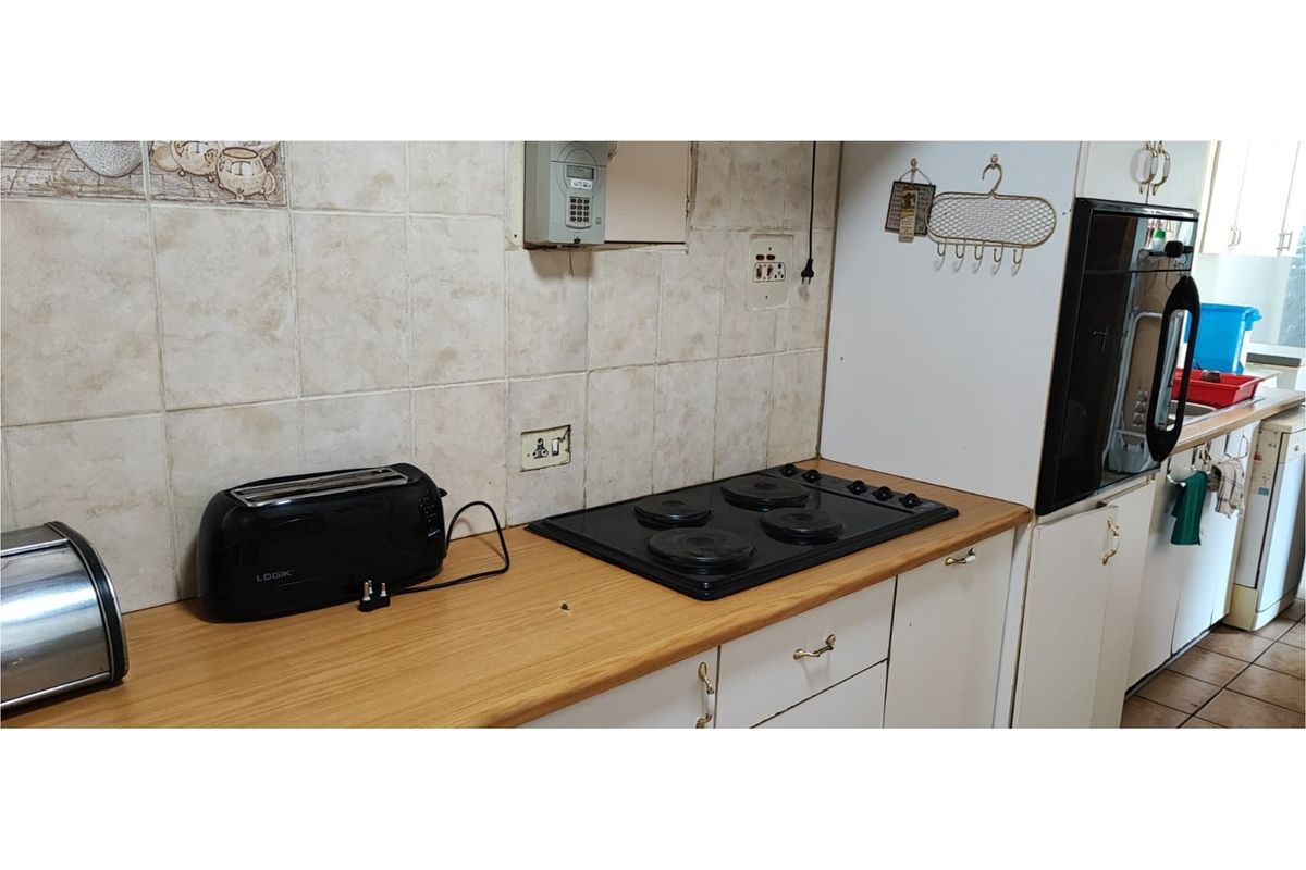 A functional kitchen area featuring a built-in electric hob, oven, laminate countertops, and tiled backsplash with ample cabinetry for storage.