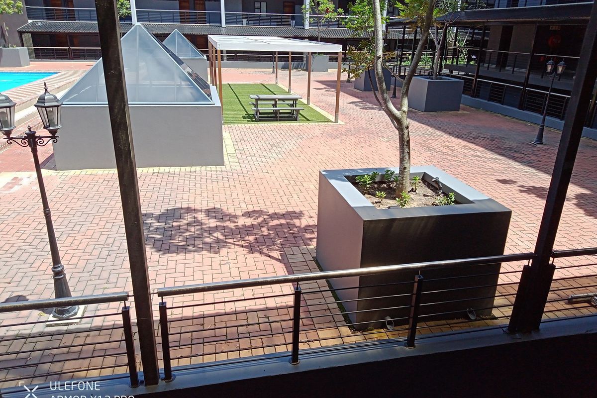 A communal courtyard area featuring paved walkways, built-in planters, a covered seating structure, and access to a swimming pool.
