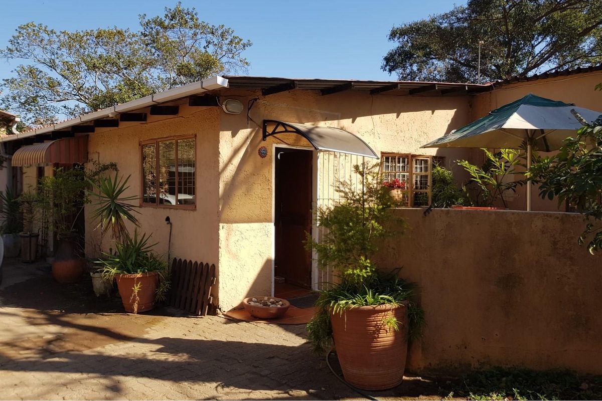 Exterior view of a small holding dwelling featuring a covered entrance, paved area, and simple architectural design.