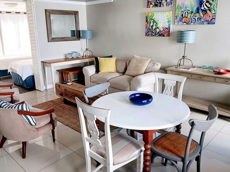 A bright living area featuring tiled flooring and an open layout with a view into the adjacent bedroom.