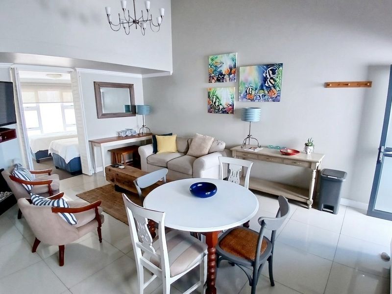 Spacious open-plan living and dining area featuring high ceilings, tiled flooring, and a bright, airy atmosphere with direct access to an adjacent bedroom.