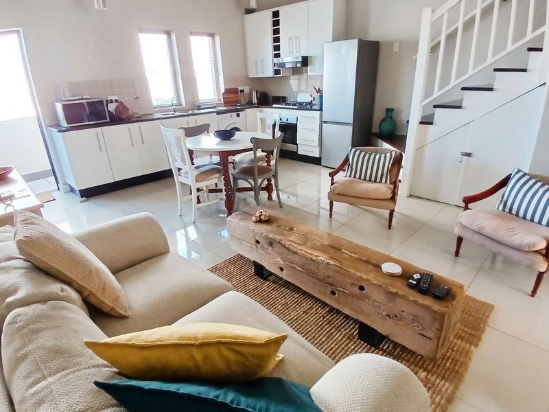 Open-plan living and kitchen area featuring tiled floors, white cabinetry, built-in appliances, and a staircase leading to the upper level.