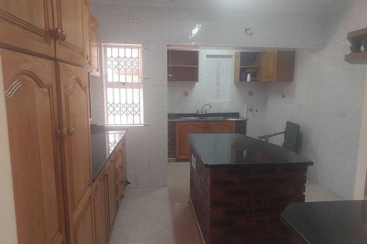 A functional kitchen featuring wooden cabinetry, granite countertops, a brick-base island, and tiled walls with a security-grilled window.