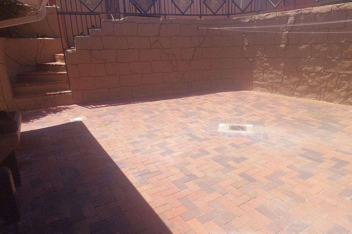 A paved outdoor courtyard area featuring a tiered retaining wall with visible structural cracking and integrated drainage.