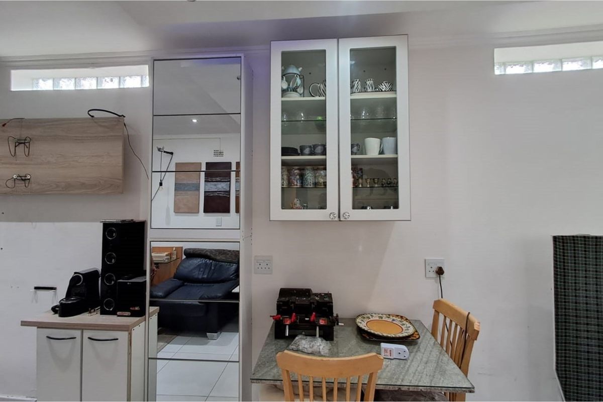 A functional kitchen area featuring built-in cabinetry, glass-fronted display cupboards, and a mirrored storage unit, providing practical storage and preparation space.