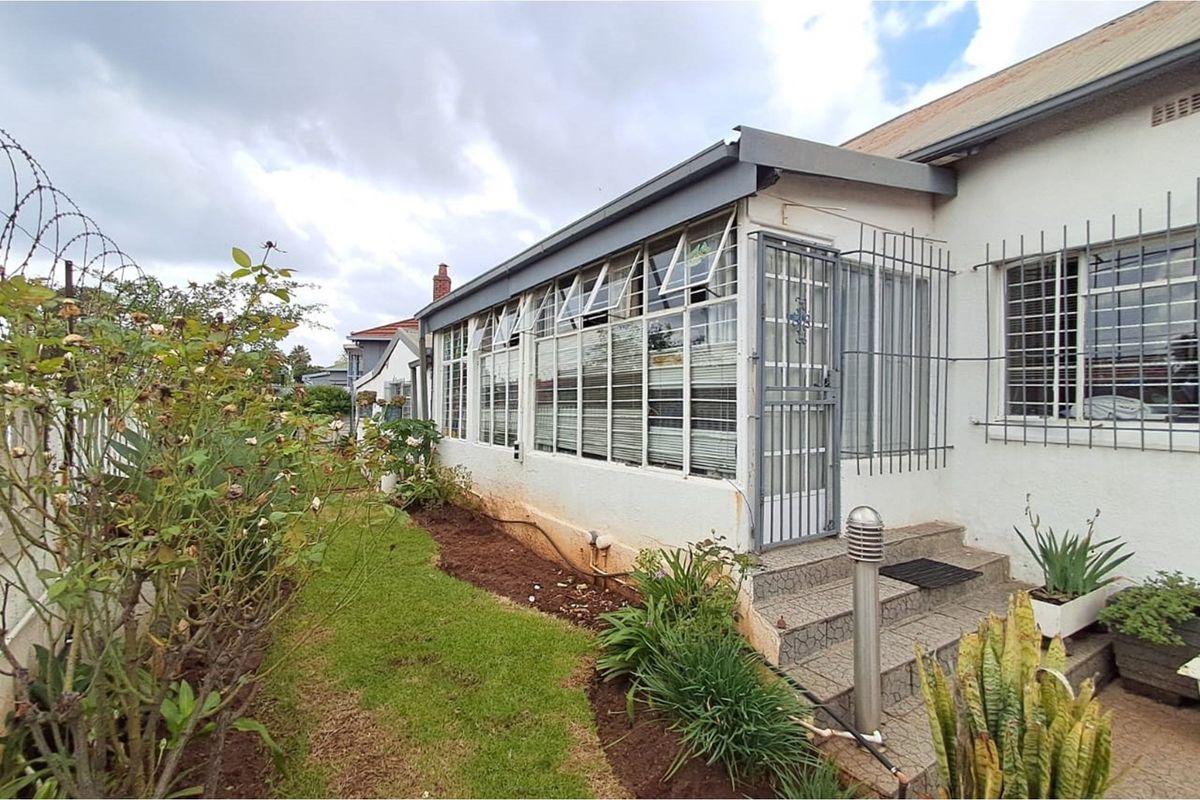 Side view of the property featuring a sunroom extension with large windows, security bars, and a small paved entrance area.