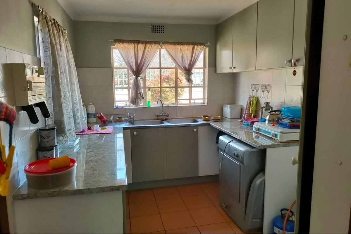 A functional kitchen featuring laminate countertops, double basin sink, wall-mounted cabinetry, and tiled flooring with space for under-counter appliances.