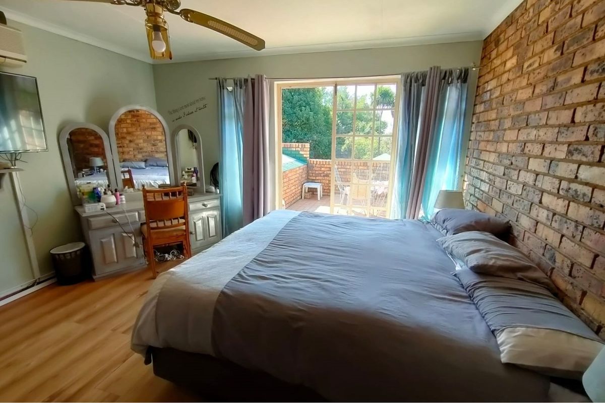 A bedroom featuring a brick feature wall, laminate flooring, and sliding glass doors providing direct access to an outdoor patio area.