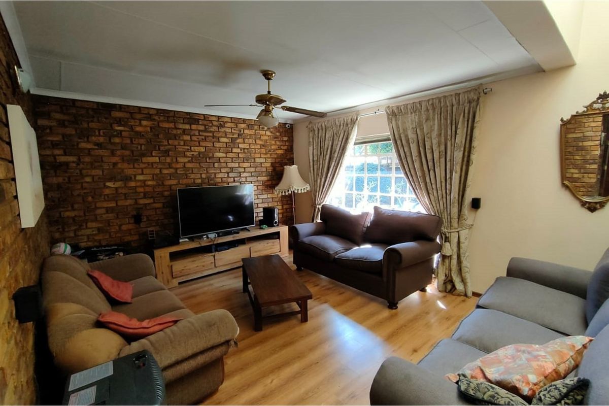 A living room featuring a prominent exposed brick feature wall, laminate flooring, and a ceiling fan.