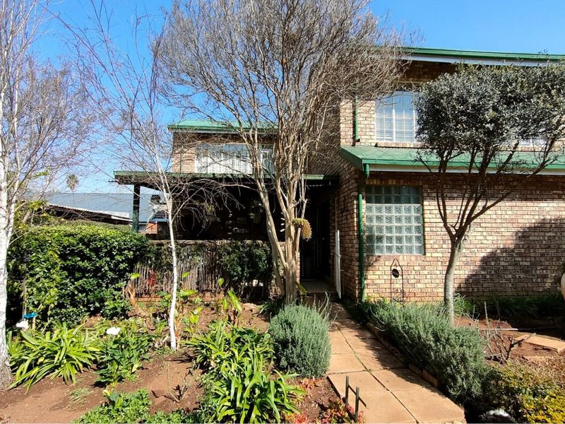 Front view of a double-story brick house featuring a covered patio, established garden, and paved walkway leading to the entrance.