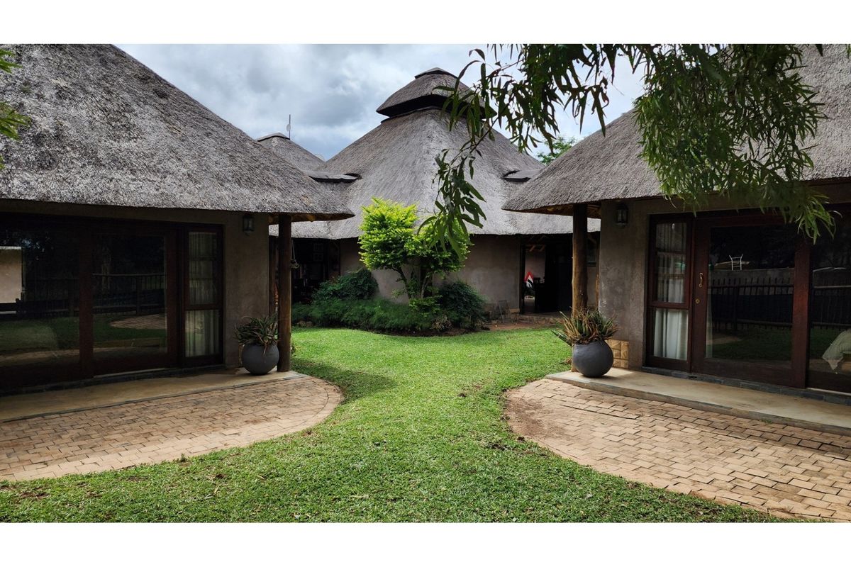 A view of the lodge exterior featuring traditional thatched roofs, brick paved patio areas, and timber structural elements set within a landscaped garden.